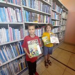 Dwaj uczniowie w bibliotece  trzymający dyplomy i książki.jpg