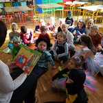 Grupa uczniów słuchających i nauczyciel czytający książkę.jpg.JPG